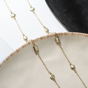 Collar minimalista dorado con dijes geométricos sobre fondo de cerámica y seda negra