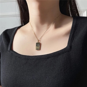 Détail d'un collier Tarot doré avec pendentif fortune porté par un mannequin en noir