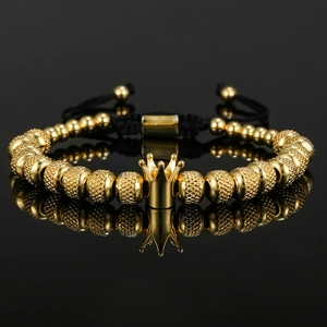 Vintage gold crown beaded bracelet with black woven adjustable strap on reflective surface