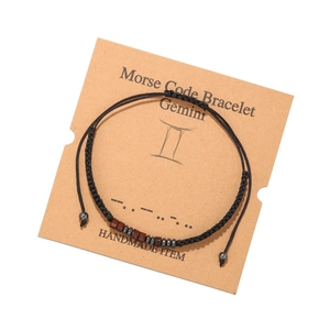 Détail du bracelet Gémeaux en code Morse avec perles de bois et cordon noir sur carte