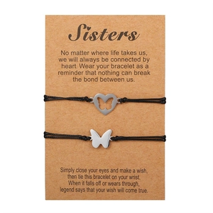 Dettaglio di due bracciali con cuore e farfalla su un biglietto regalo Sisters marrone