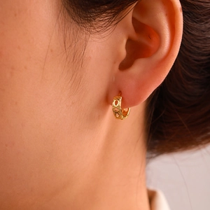Dettaglio degli orecchini huggie placcati in oro con design geometrico a 'X' e cerchi