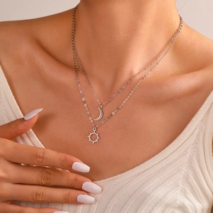 Close-up of layered stainless steel necklaces with moon and sun charms worn by a model