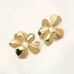 Elegant gold flower earrings with white pearls for women on white textured fabric background