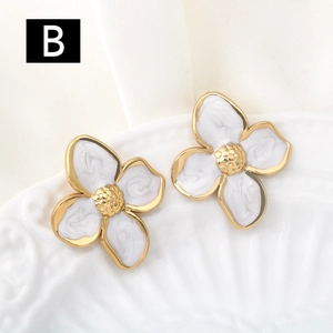 Detailed macro view of gold flower earrings with white enamel marble texture