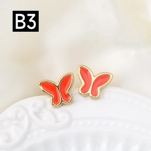 Detalle de pendientes de mariposa dorados con incrustaciones de esmalte rojo vivo