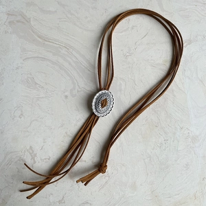 Westerse Bolo Tie met zilveren ovale hanger en bruin suède koord op marmeren blad