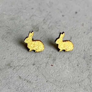 Goldene Hasen-Ohrstecker im minimalistischen Design auf grauem Stein-Hintergrund