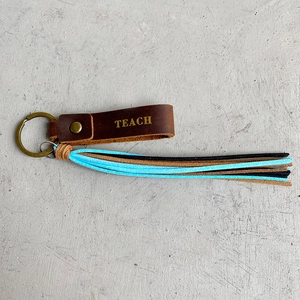 Macro detail of crazy horse leather keychain with TEACH gold foil stamping and tassels