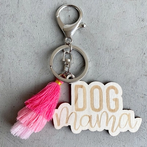 Détail du porte-clés en bois Dog Mama avec pompon rose sur une surface en pierre
