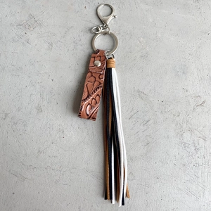 Macro detail of vintage embossed brown leather keychain with tricolor tassel and metal hook