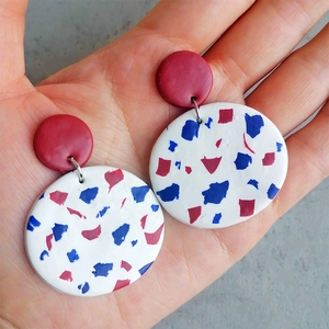 Detail of red and white terrazzo pattern handmade clay earrings held in hand for scale