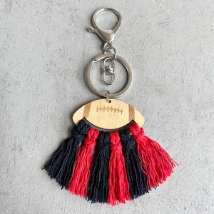 Close-up of handmade football wooden keychain with red and black macrame tassel