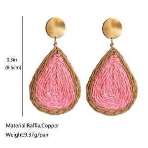 Detailed view of teardrop woven raffia earrings with golden studs and pink contrast