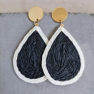 Detail of woven teardrop raffia earrings with gold studs on a textured stone background