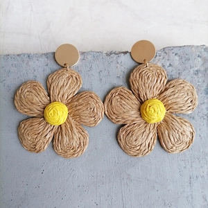 Detailed close-up of woven raffia flower earrings with yellow centers on stone