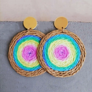 Detail view of woven rainbow earrings with gold stud on grey stone surface