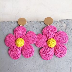 Detailed macro view of handmade pink raffia flower earrings with golden metal studs