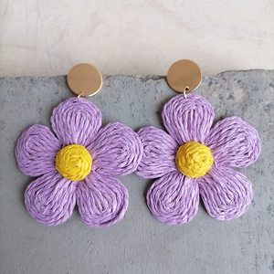 Detail of bohemian raffia flower earrings in purple and yellow on a stone surface