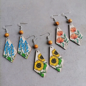 Detalle de pendientes boho de madera con girasoles y motivos florales pintados a mano