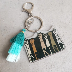 Close-up of Be Kind acrylic keychain with triple-layered green cotton tassel detail