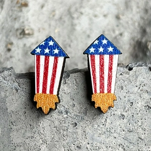 Detail of wooden rocket earrings with American flag patterns and gold glitter accents