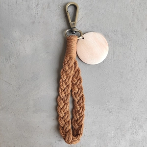 Detail of handmade braided wristlet keychain with wood tag on gray cement background