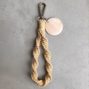 Detail of bohemian handmade woven keychain with beige rope and round wooden tag charm