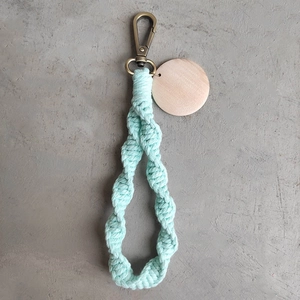 Close-up of mint green macrame keychain with wooden tag and bronze lobster clasp