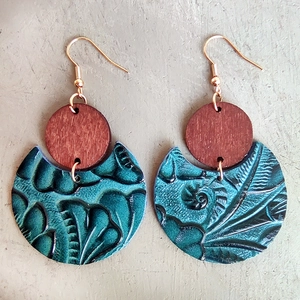 Detail of vintage boho leather earrings with wooden disk and embossed teal pendant