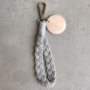 Detail view of handmade grey macrame keychain with bronze clasp and blank wooden tag