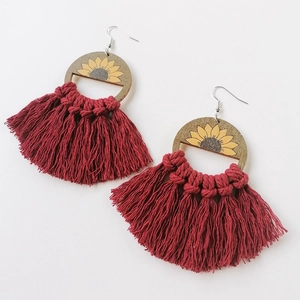 Detail of bohemian fan-shaped earrings with wooden sunflower disks and dark red cotton tassels