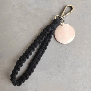 Détail d'un porte-clés en macramé noir avec étiquette en bois et fermoir mousqueton bronze
