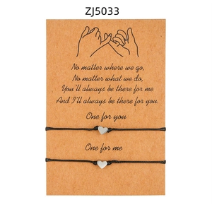 Dettaglio di due braccialetti di coppia intrecciati con ciondoli a cuore su carta