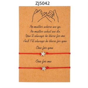 Dettaglio di braccialetti rossi intrecciati per coppia con ciondoli a stella su carta regalo