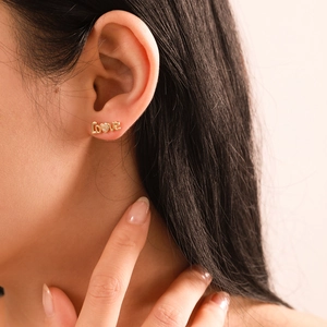 Orecchino a lobo dorato Love con zircone a cuore indossato da modella su sfondo rosa