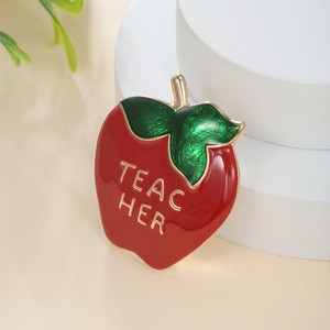 Detail of red apple enamel brooch with gold Teacher text on a white pedestal