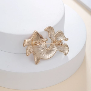 Detail view of gold metal brooch back showing textured finish and safety pin clasp
