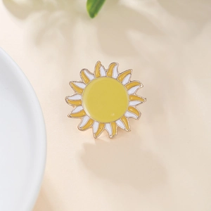 Detail of a bright sun enamel brooch with golden trim and wave rays on a beige background