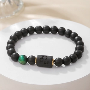 Detalle macro de la pulsera del signo Leo en negro mate con cuenta verde y piezas doradas