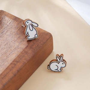 Detalle de pendientes de madera con forma de conejo sobre soporte de madera y tela beige