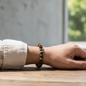 8mm tiger eye bead bracelet with cylindrical metal charm on a male wrist over wood