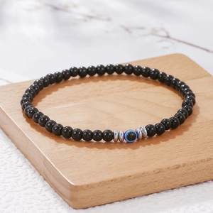 Detailopname van een 4mm zwarte kralenarmband met blauw boze oog kraal op houten plank