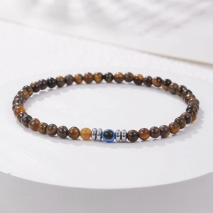 Macro-opname van 4mm tijgeroogkralen en blauwe evil eye bedel aan een elastische armband