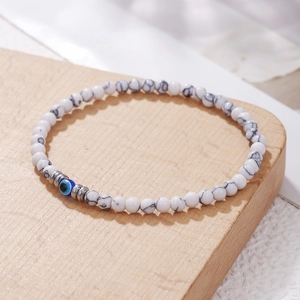 Detailopname van witte marmeren kralen en blauwe evil eye bedel op elastische armband