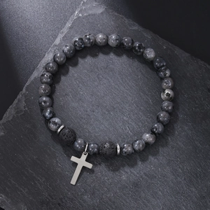 Detalle de pulsera de cuentas de piedra con cruz de plata sobre base de pizarra oscura