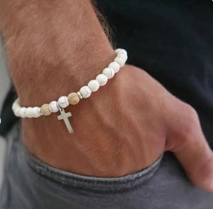 Detalle de pulsera de cuentas de mármol blanco con colgante de cruz plateada en muñeca