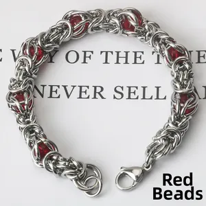 Close-up of industrial woven steel bracelet with lobster clasp and red bead accents