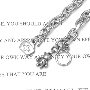 Macro shot of stainless steel chain bracelet with bear and nurse hat charms and T-bar clasp