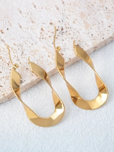 Detailed view of gold twisted U-shaped earrings with polished finish on a stone surface